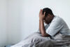 Depressed young black men sitting in bed hiding head in hands, having headache